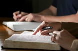 Couple studying the Holy Bible together at a table (shallow focus side lighting).